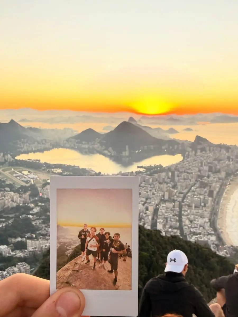 A polaroid of the hiking group held up against the sunrise view over Rio de Janeiro