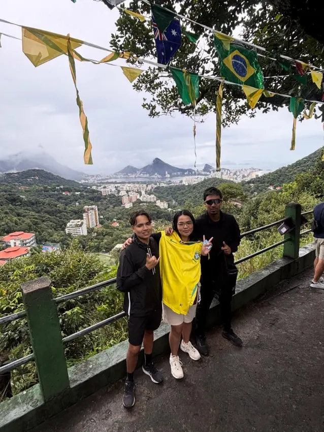 Guides and a traveller holding up a Brazil football jersey at a viewpoint decorated with flags