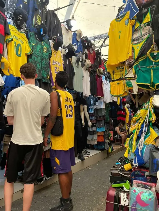 Travellers browsing football jerseys at a street market stall