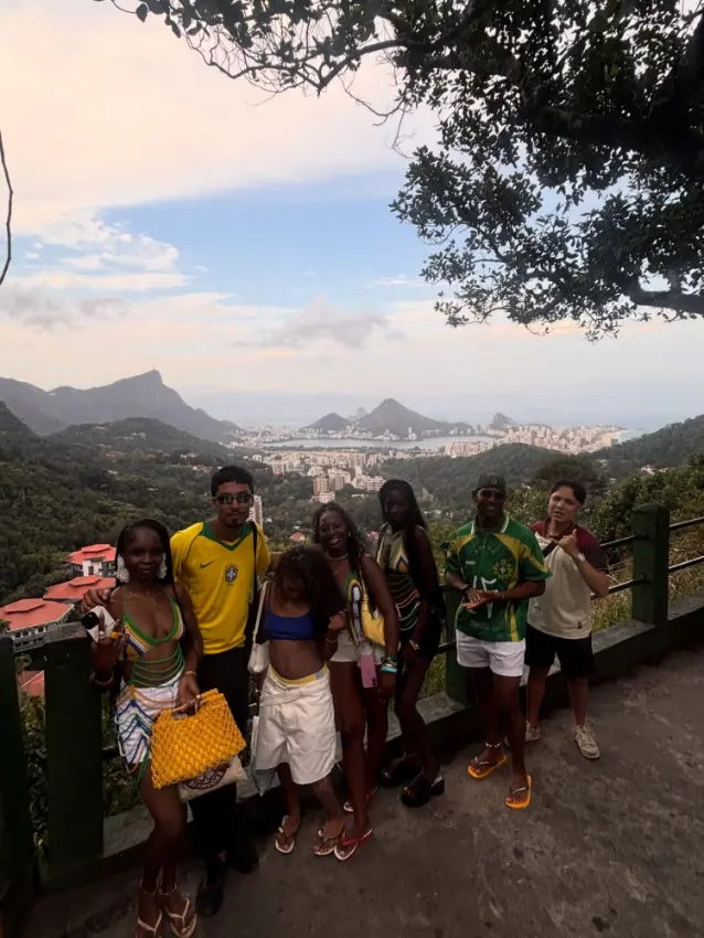 Travellers in Brazil shirts at a viewpoint at golden hour, with Christ the Redeemer and Sugarloaf Mountain behind them