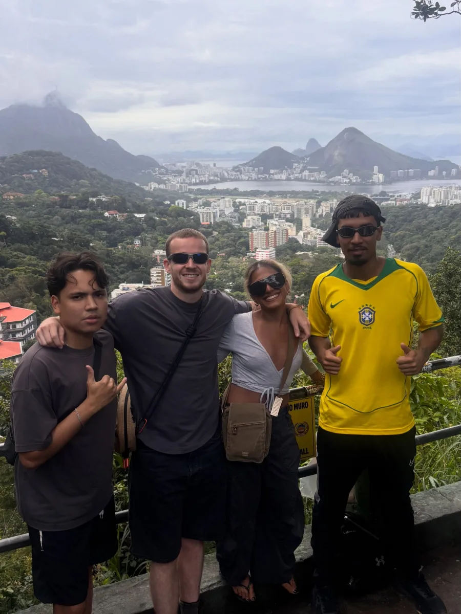 Four people arm in arm at a viewpoint above Rocinha, the Lagoa and Corcovado behind them